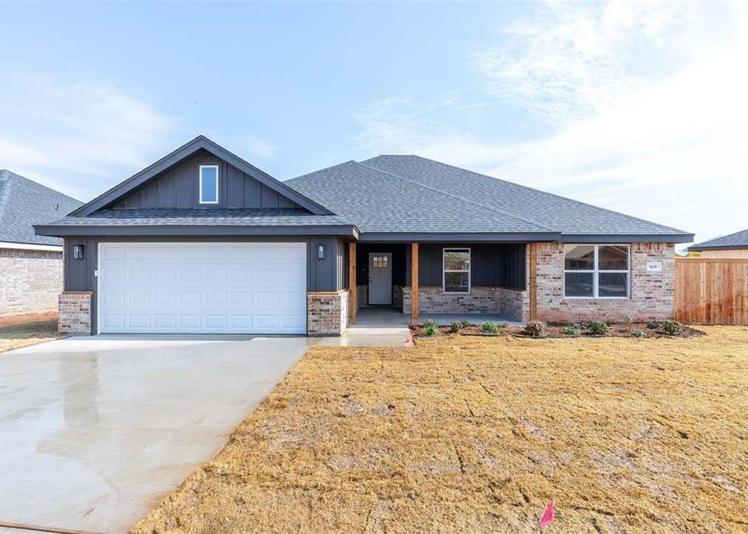 Newly built house with a concrete driveway, grass front yard, brick and dark siding exterior, and a front porch with a wooden post.