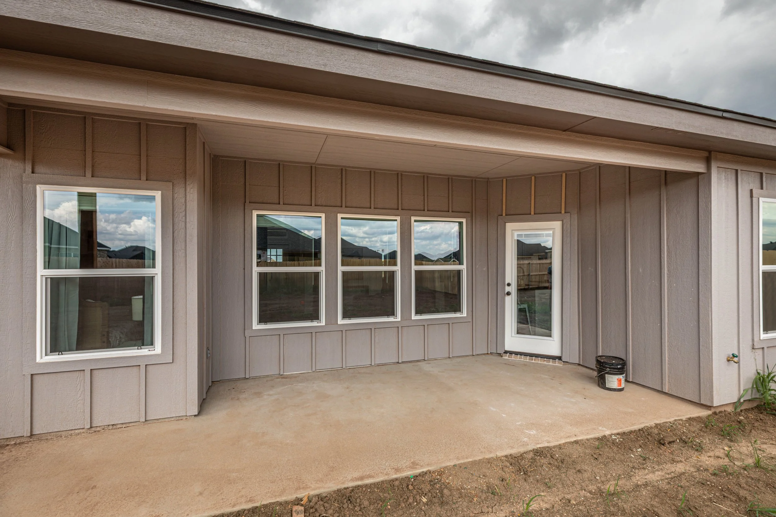 Rear view of a house with sliding glass doors, double-hung windows, and a covered patio area under a cloudy sky.