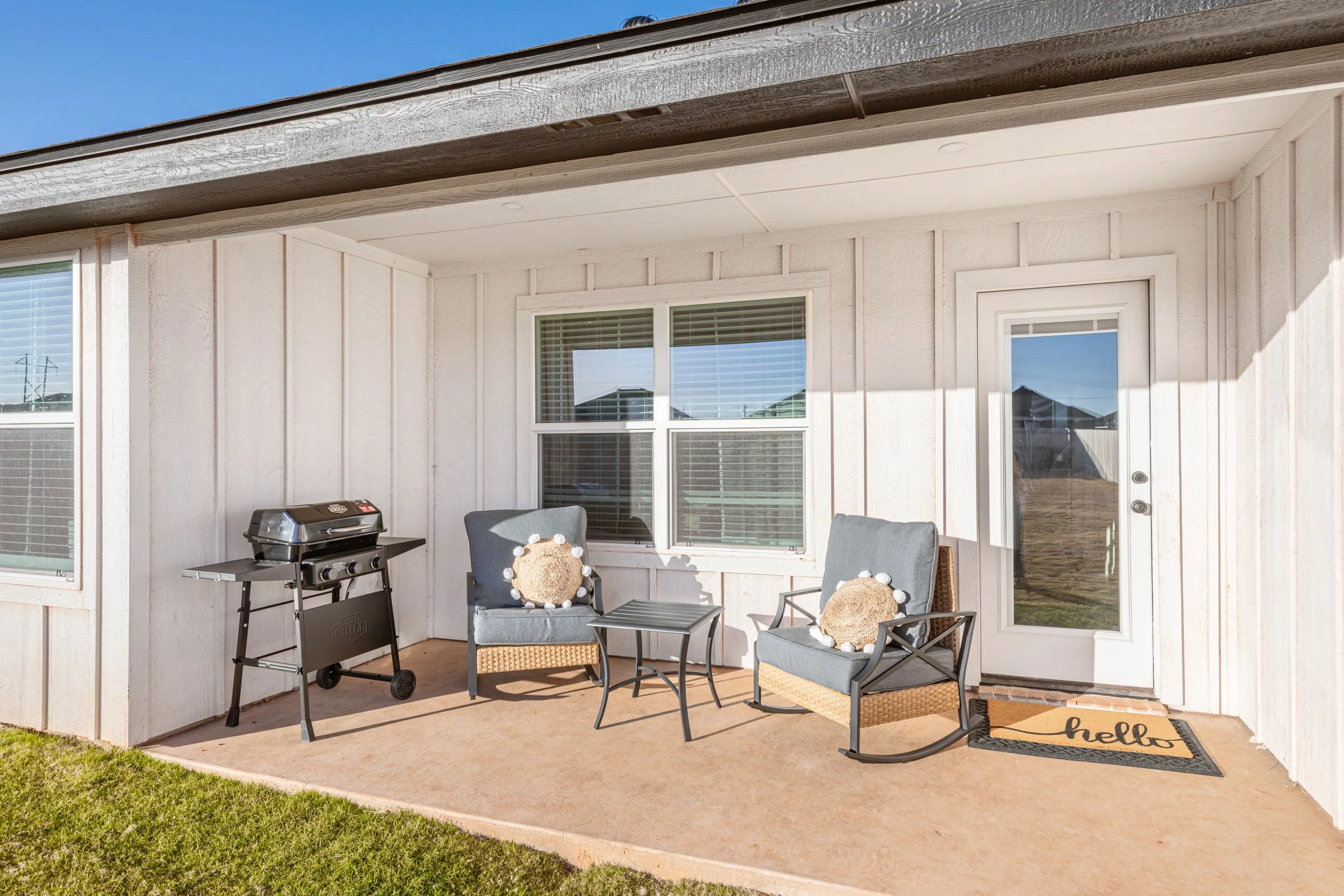 Back porch of a house with patio furniture, a grill, and a welcome mat that says 'hello'.