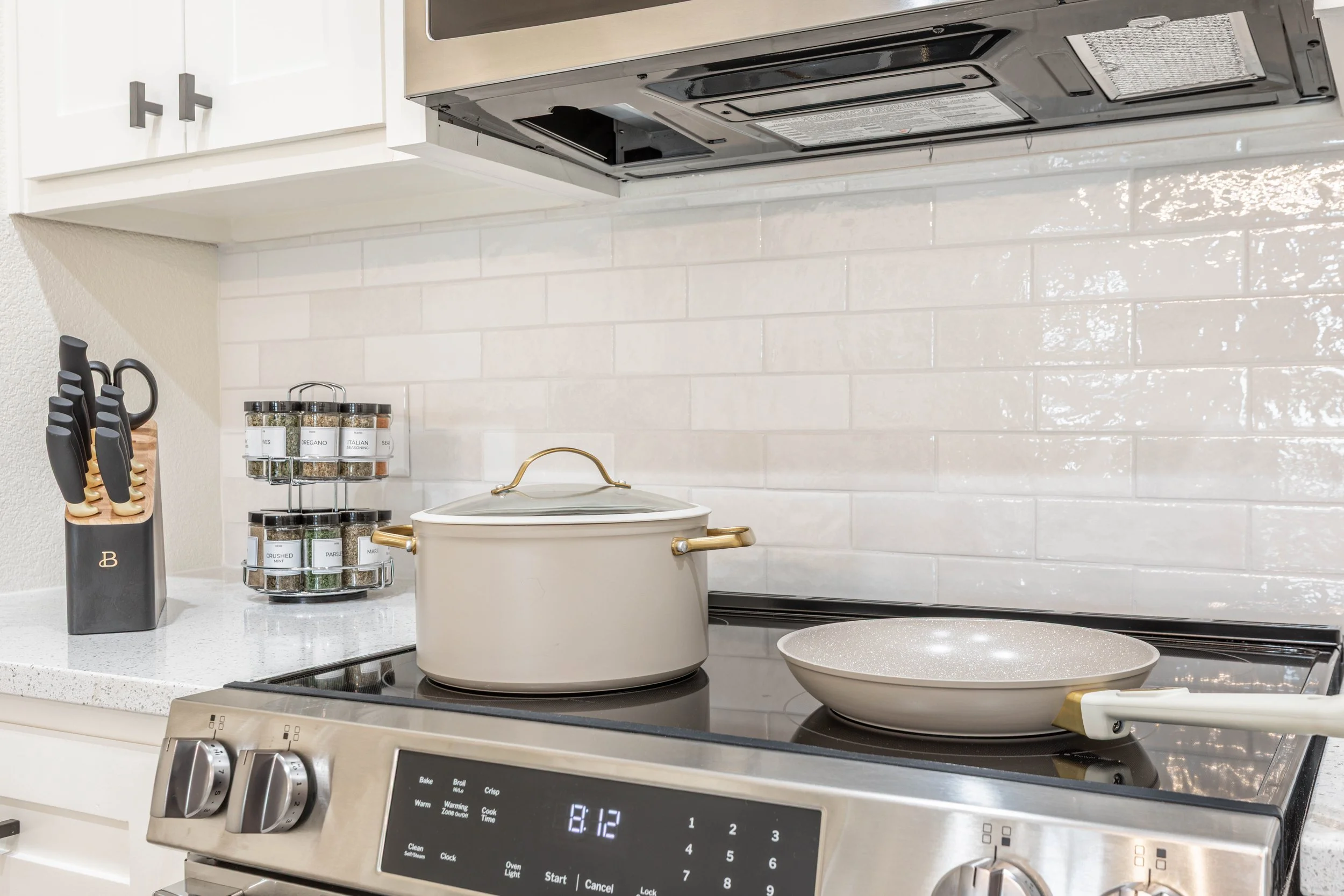 A kitchen stove with a pot on it, a spice rack with labeled spice jars, and kitchen utensils in a knife holder.