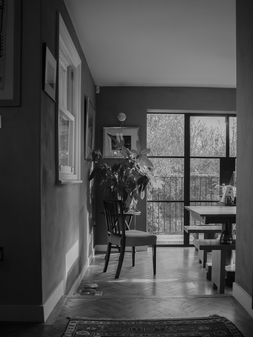 Interior view of a cozy living space with a large window, potted plant, chairs, and artwork in black and white.