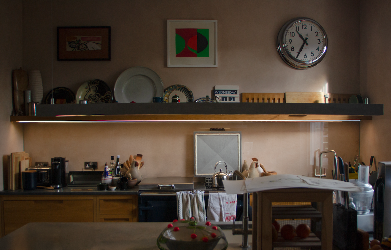 Kitchen with dishes on open shelf, a wall clock, and various kitchen appliances and utensils.