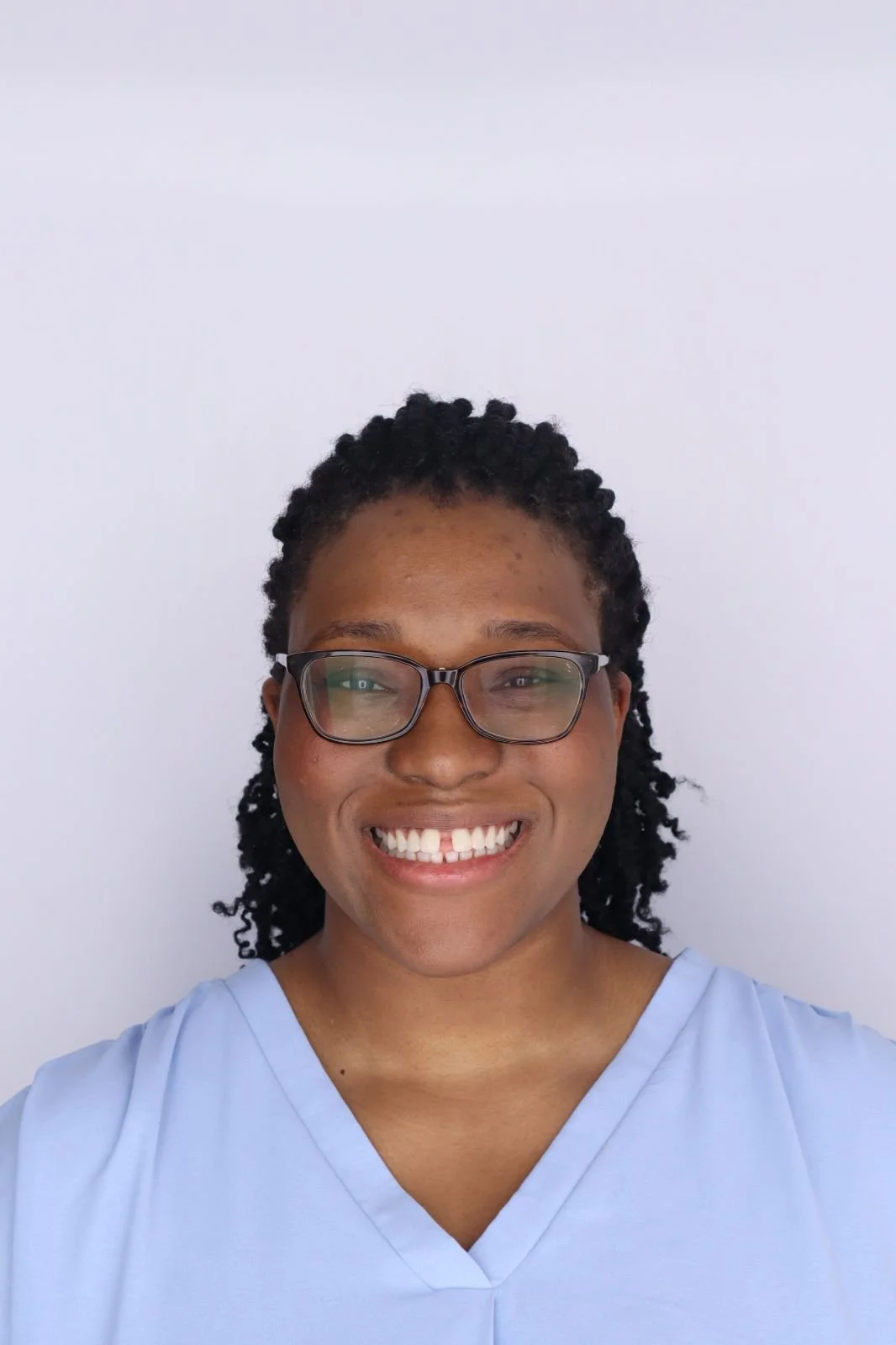 A smiling woman, a tutor, with glasses in a light blue blouse against a plain white background.