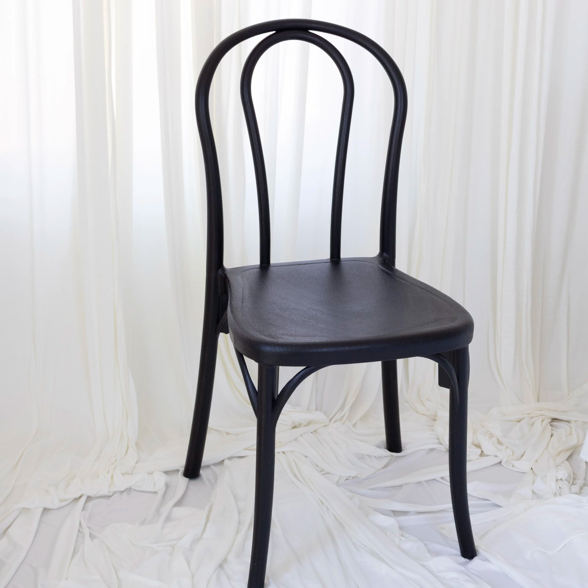 Black chair with curved backrest and textured seat, set against white ruffled backdrop.