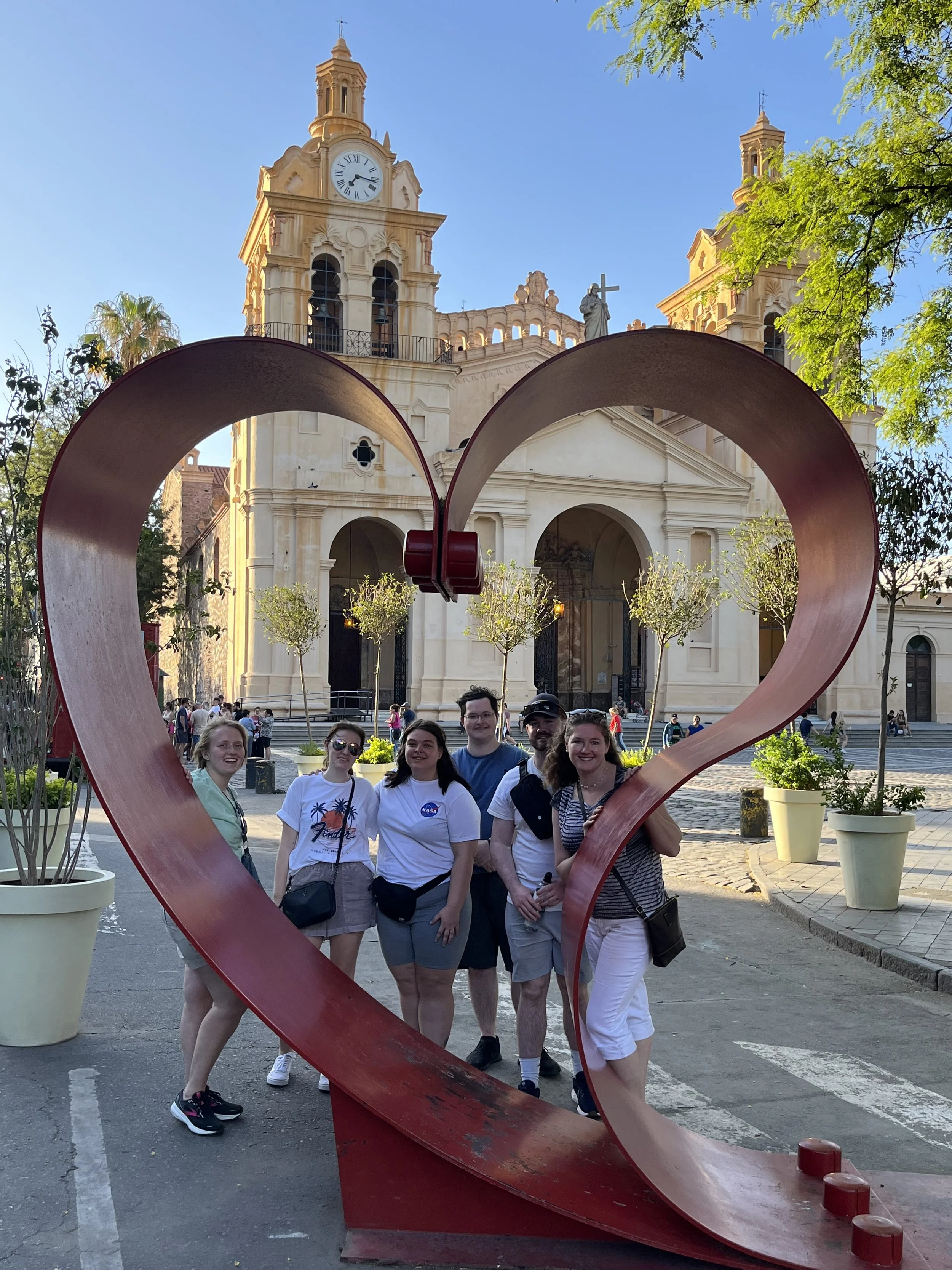 Six people posing in a heart sculpture with the Cordoba, Argentina cathedral in the background. Shane is on the far right and the others are students.