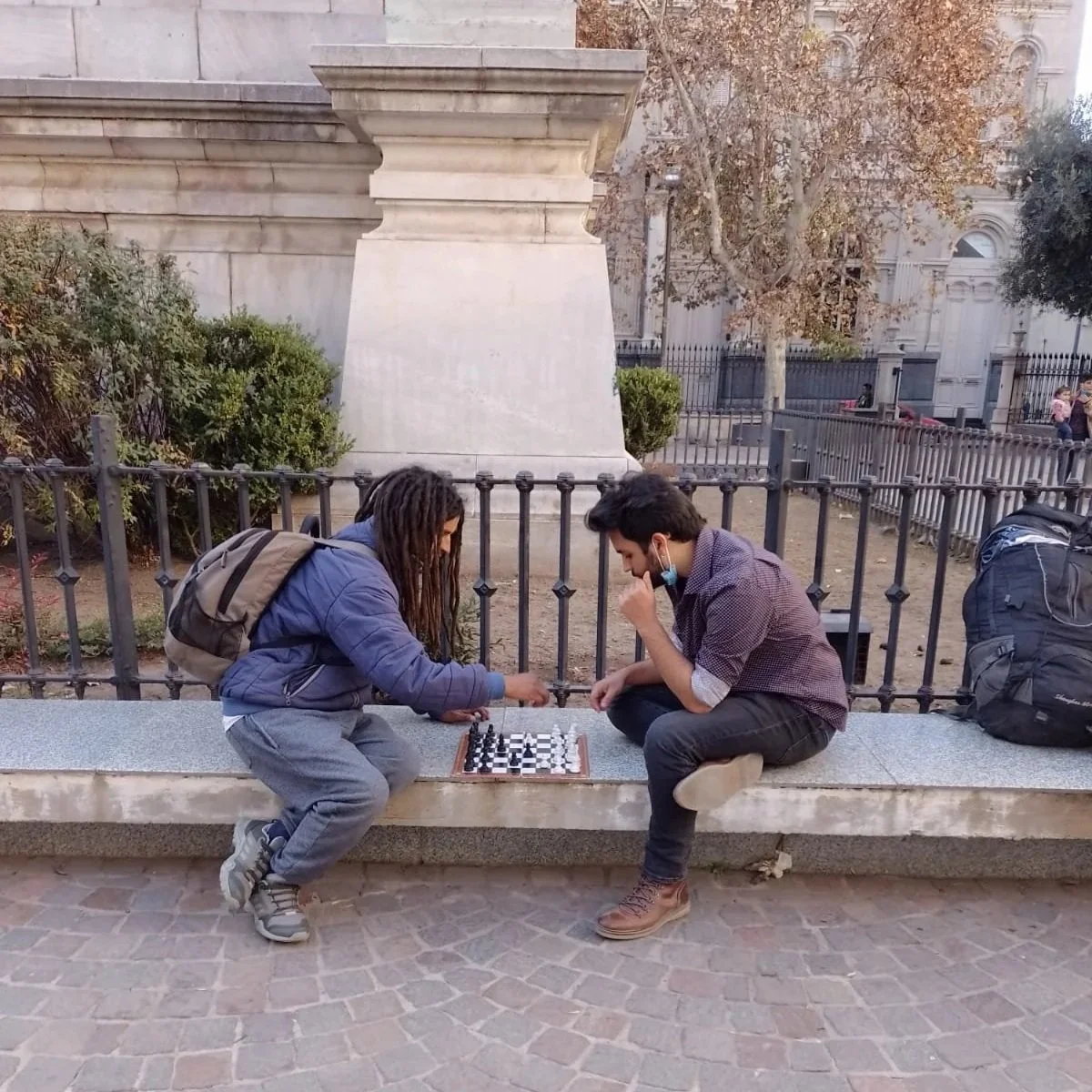 Two men sit outside playing chess.