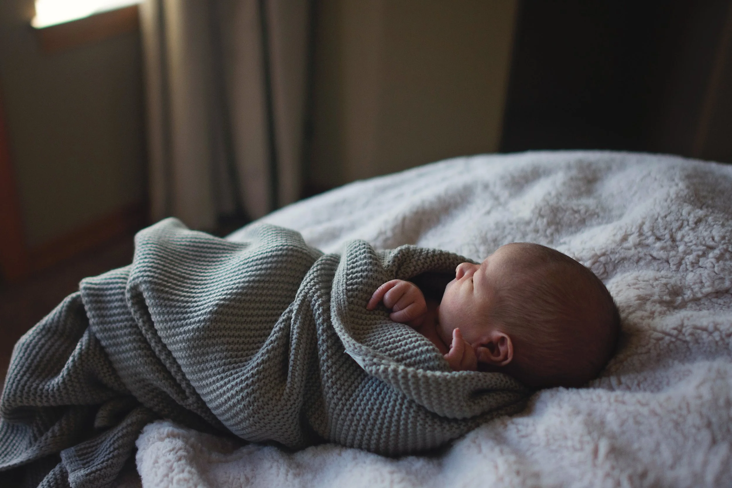 A newborn baby lying on a blanket, dressed in a striped knit outfit, resting peacefully with one hand near the face.