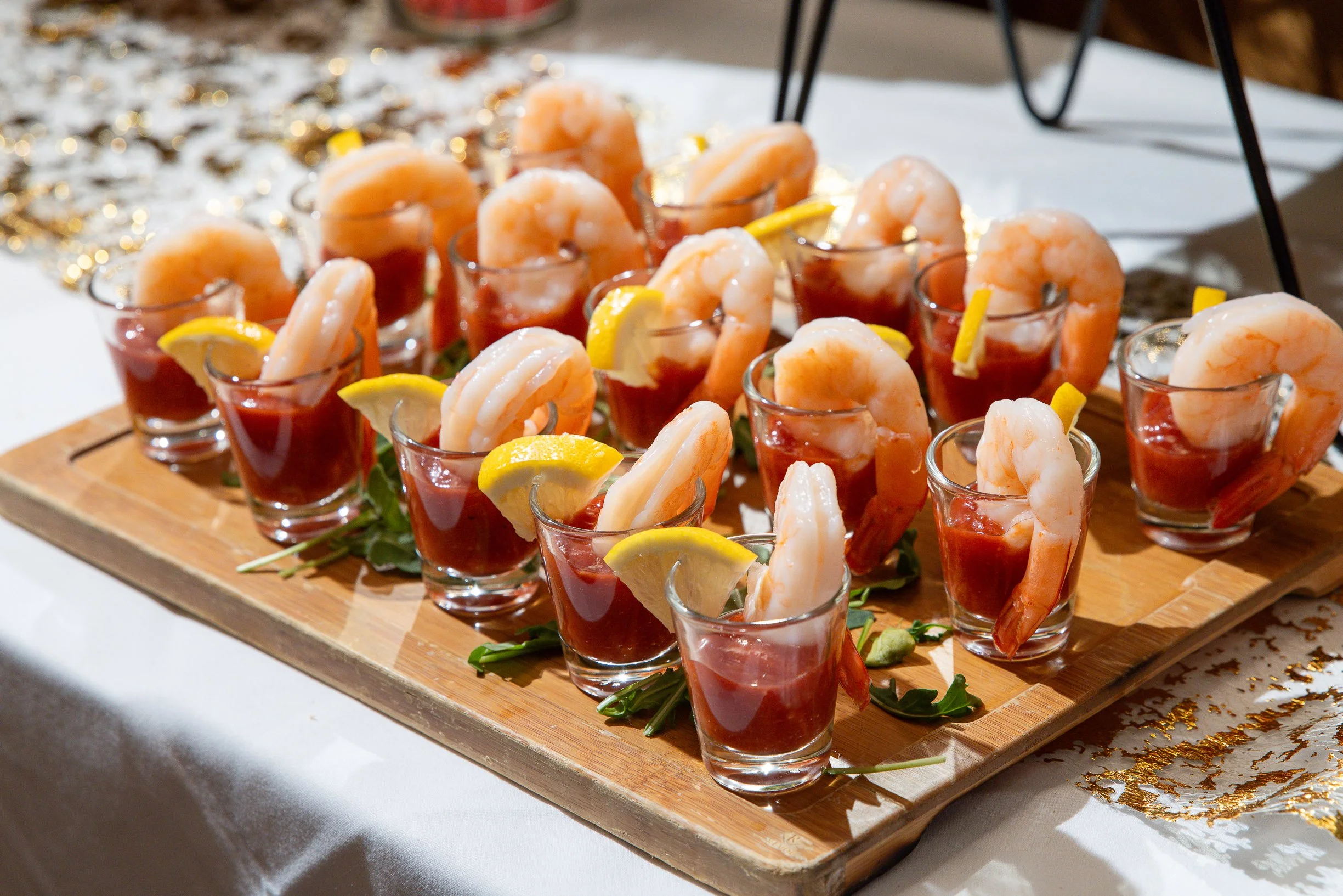 Small glass cups filled with shrimp and red sauce, garnished with lemon wedges, arranged on a wooden tray