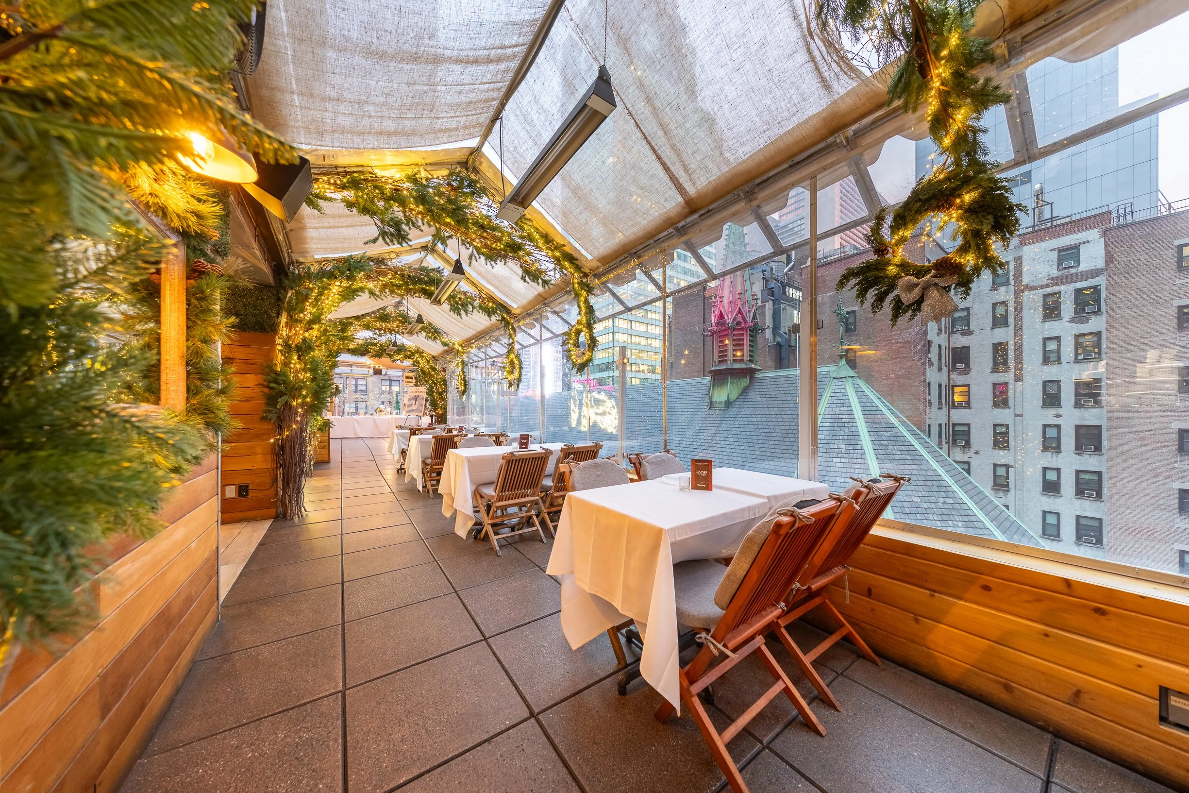 Indoor restaurant with decorated ceiling garlands and view of city buildings outside.