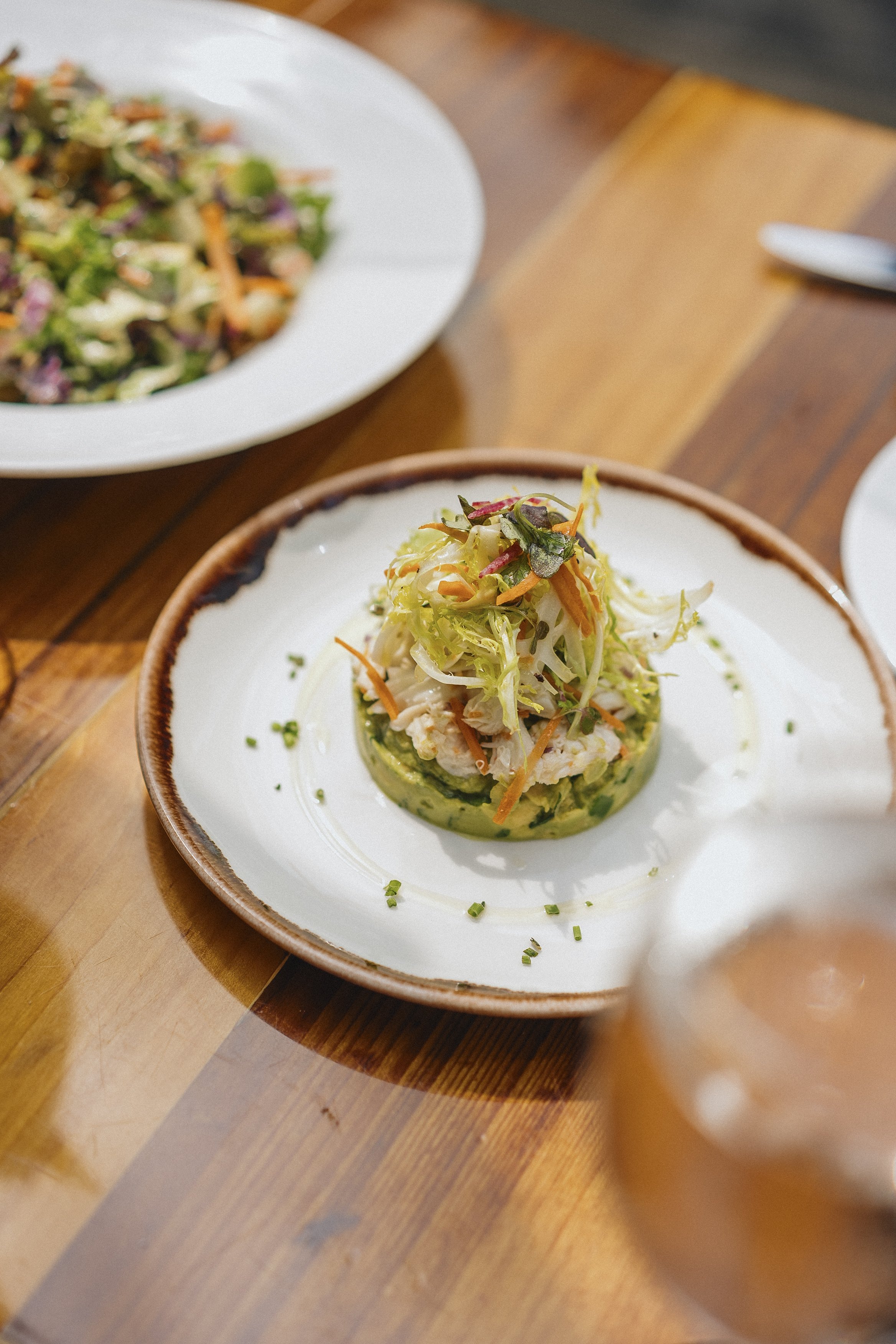 A plate of a salad with shredded lettuce, carrots, and herbs on a wooden table.