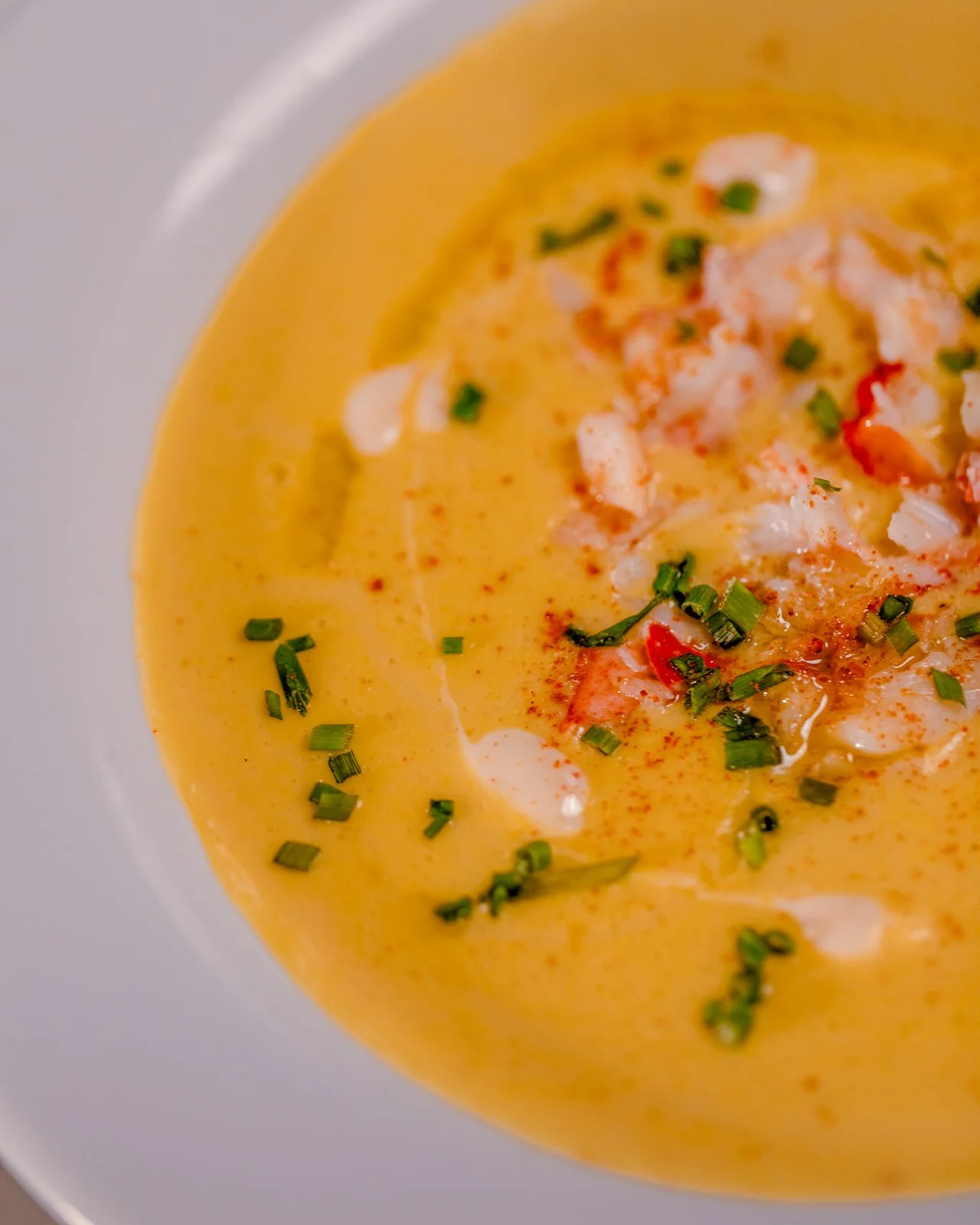 Close-up of creamy lobster bisque garnished with chopped green onions and a sprinkle of red spices.