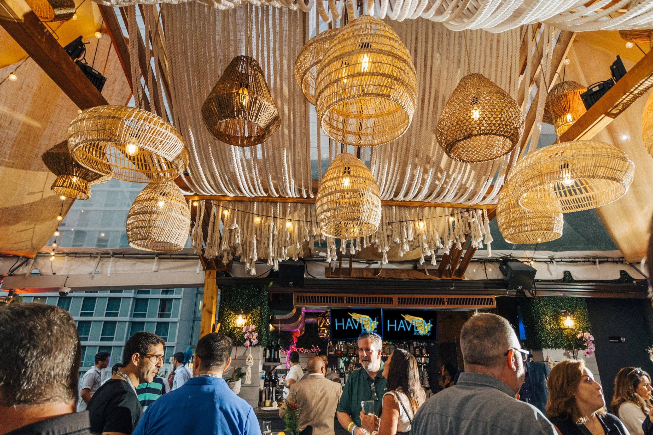 Crowd of people gathered at an indoor event with woven rattan pendant lights and string lights hanging from the ceiling.