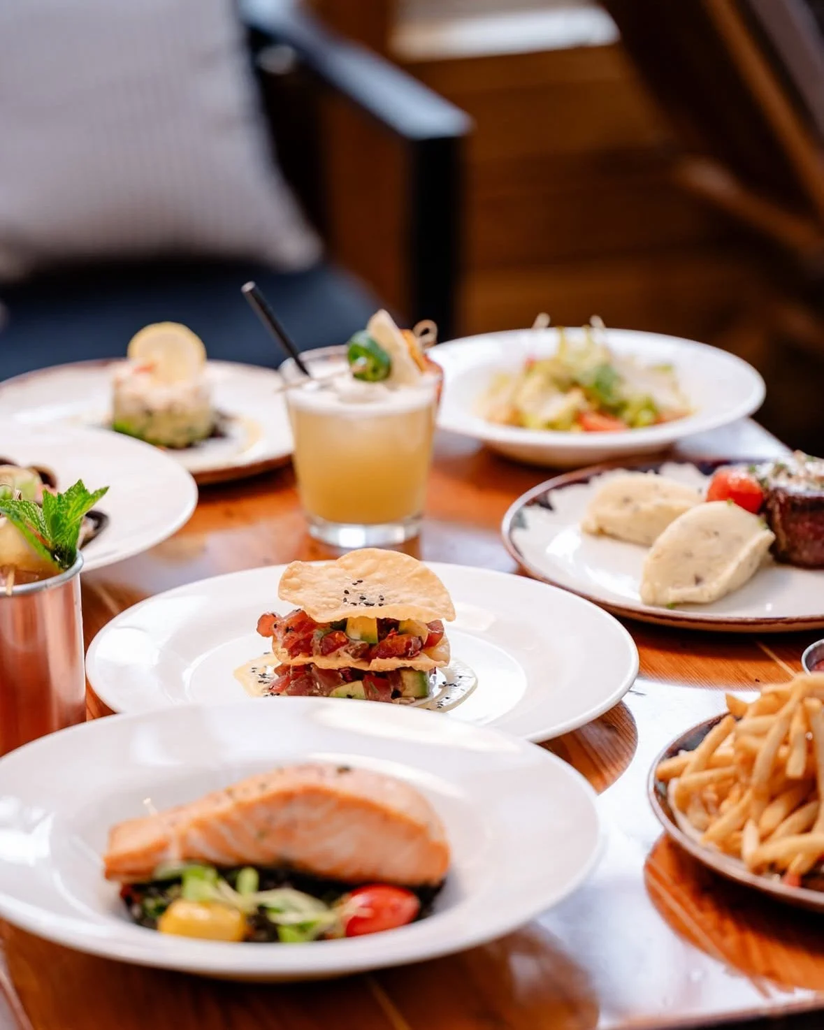 A variety of dishes on a dining table, including salads, a glass of cocktail, pasta, and grilled salmon.