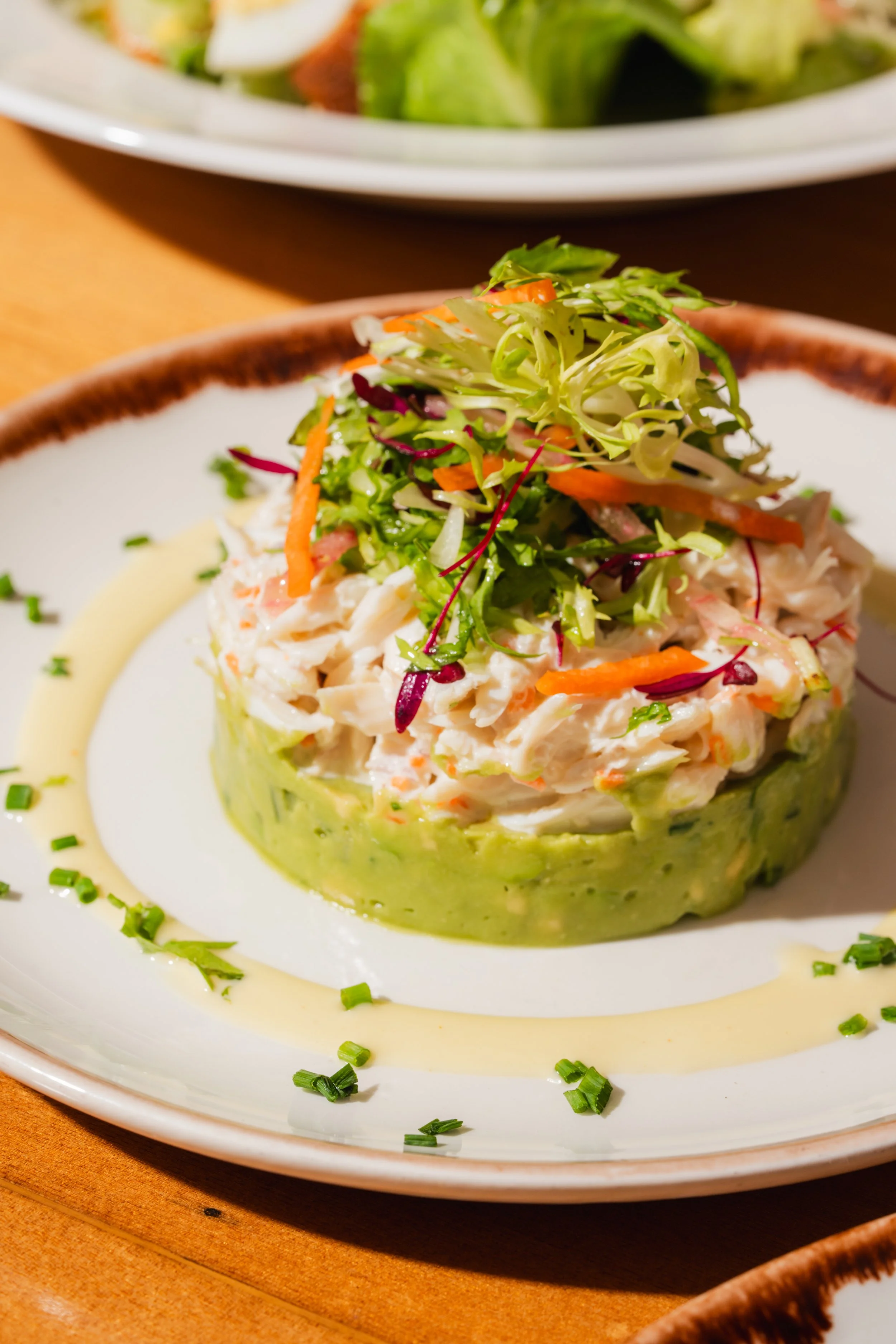 A plated dish with a green, hollowed-out vegetable topped with shredded salad and garnished with chopped herbs, served with a creamy sauce on a white plate.