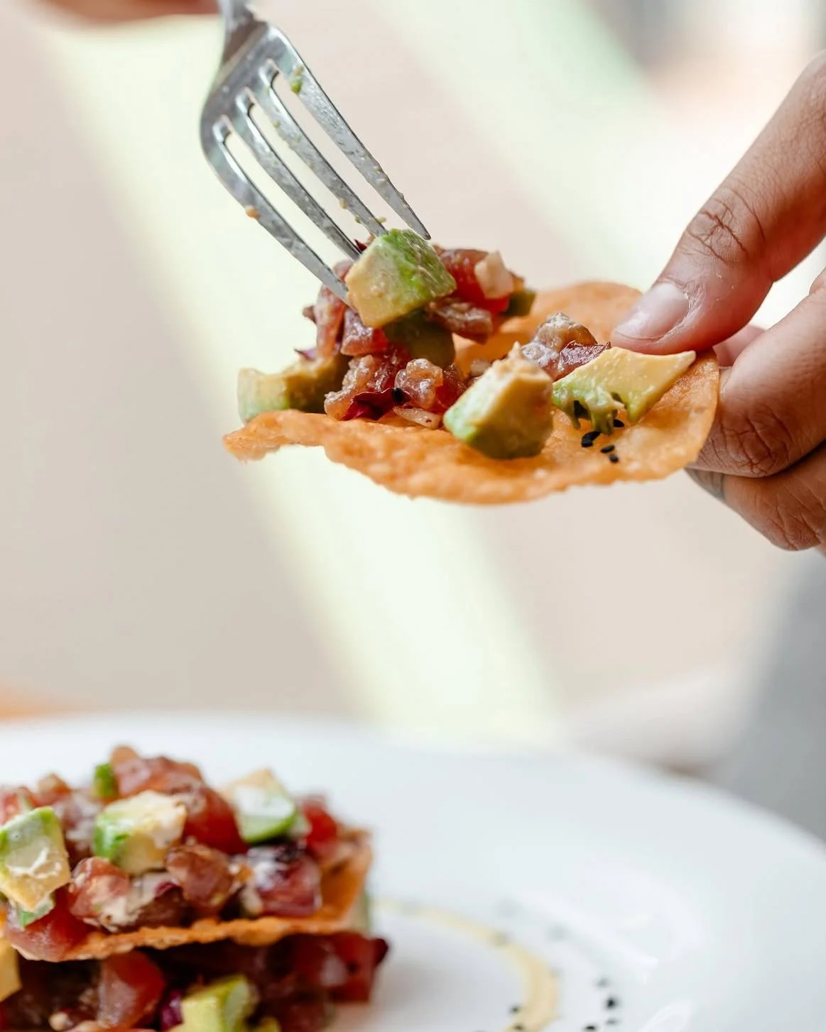 A person is holding a crispy chip with diced avocado and pico de gallo on top, with another chip in the background.