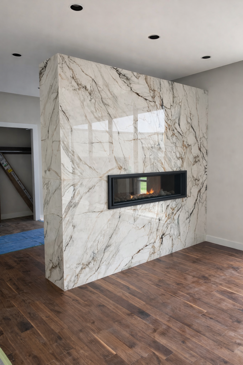 A marble fireplace wall with a modern rectangular gas fireplace, in a room with wooden flooring and a gray ceiling with recessed lights.