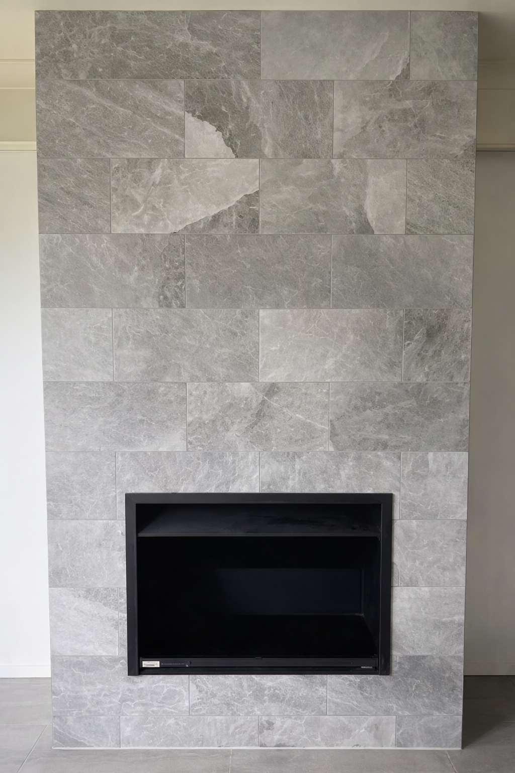 Interior view of a modern fireplace with a black interior, surrounded by a wall of large gray stone tiles.