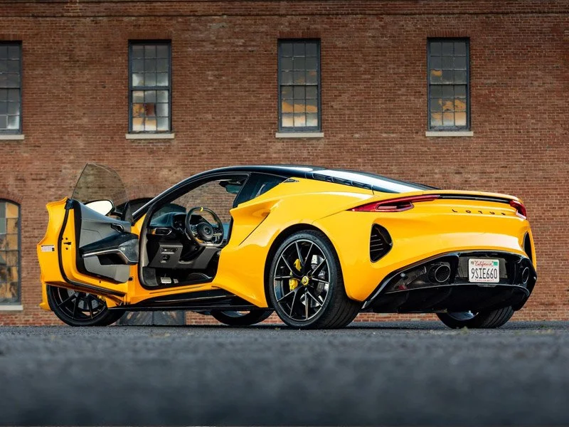 Yellow Lotus Emira with open door parked on street in front of a brick building with windows which was sold on Cars&Bids and had the sale managed by KennanR who brought 10% more than market value by representing the car professionally