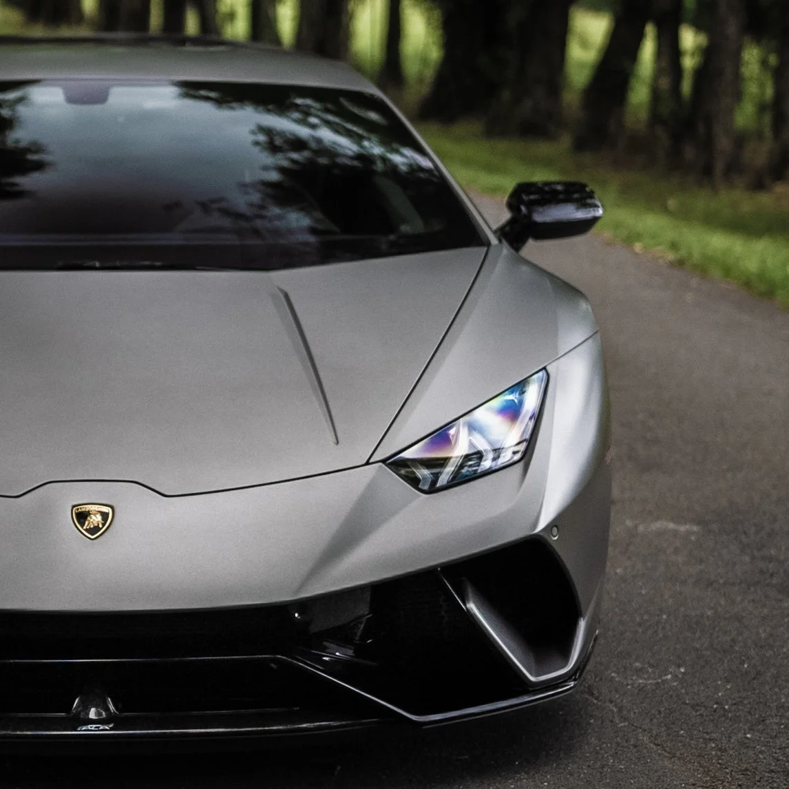 Close-up of a gray Lamborghini Huracan Performante parked on a road with a forest background.