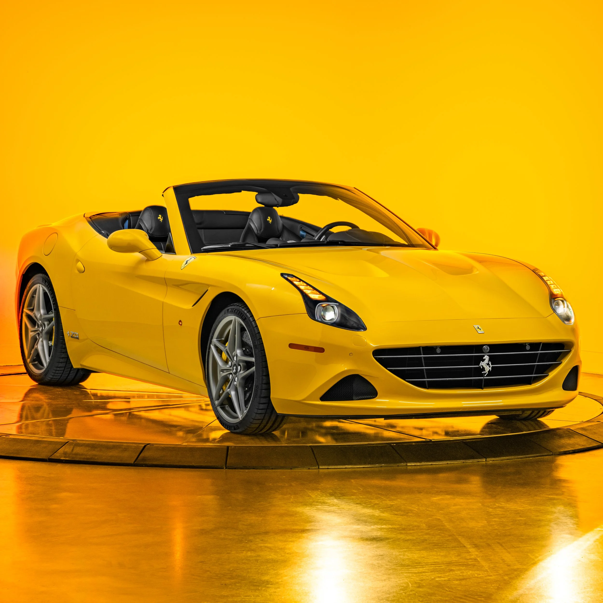 A Giallo Triplo Strada Ferrari California T 70th Anniversary with a black interior set against a bright yellow background.
