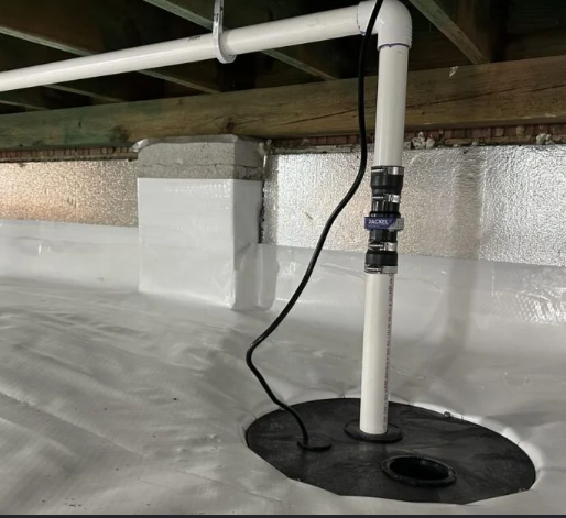 A plumbing system with a white PVC pipe, a black flexible pipe, and a black rubber gasket on a white waterproof surface inside a building's crawl space.