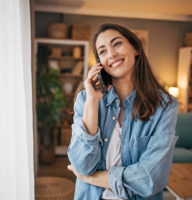 Young woman smiling and talking on her mobile phone in a cozy home setting.