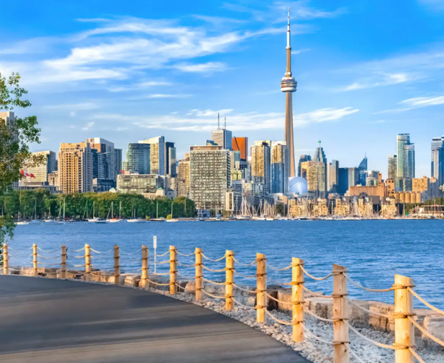 Toronto skyline with CN Tower across a body of water, with a promenade and rope fence in the foreground.