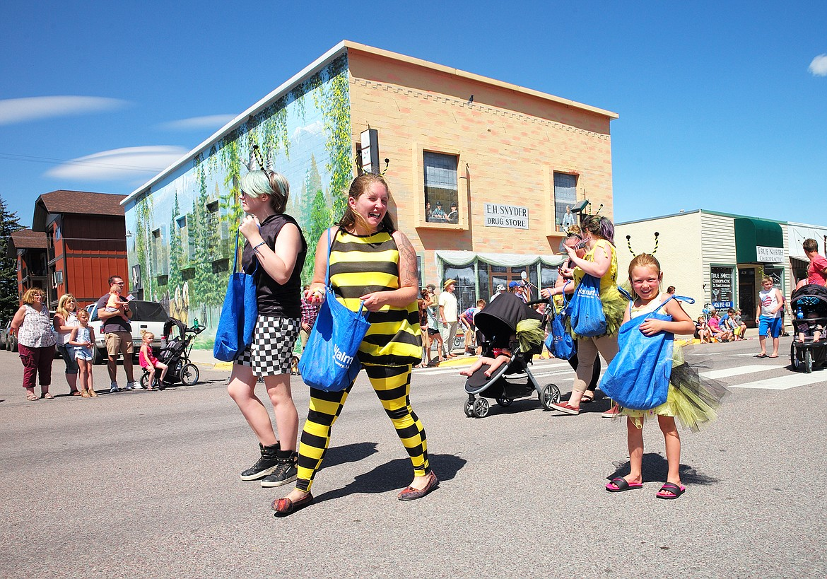 People dressed as bees walking on a street during a parade or event, with a crowd of onlookers and shops in the background.