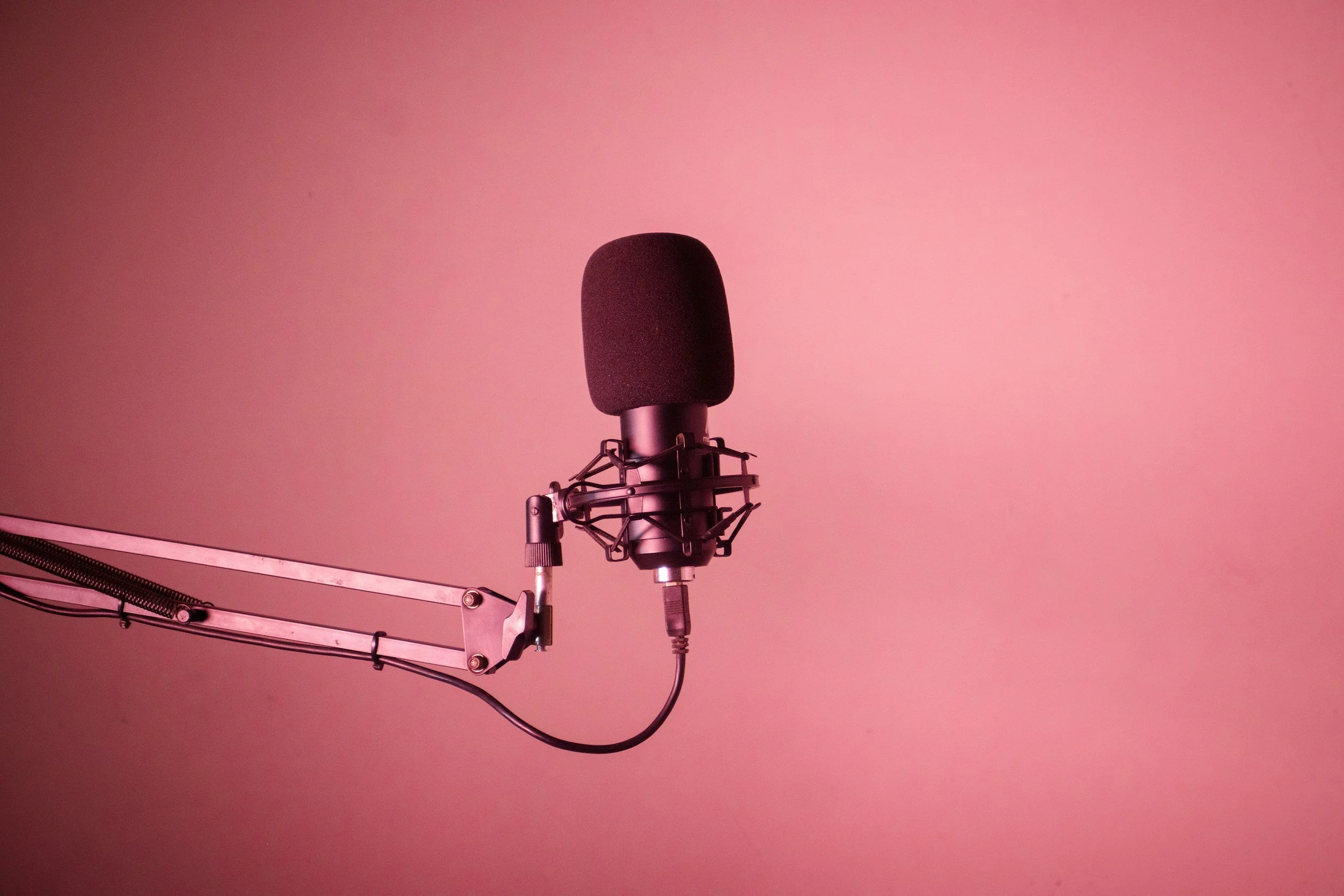 A professional studio microphone mounted on an adjustable arm against a pink background.