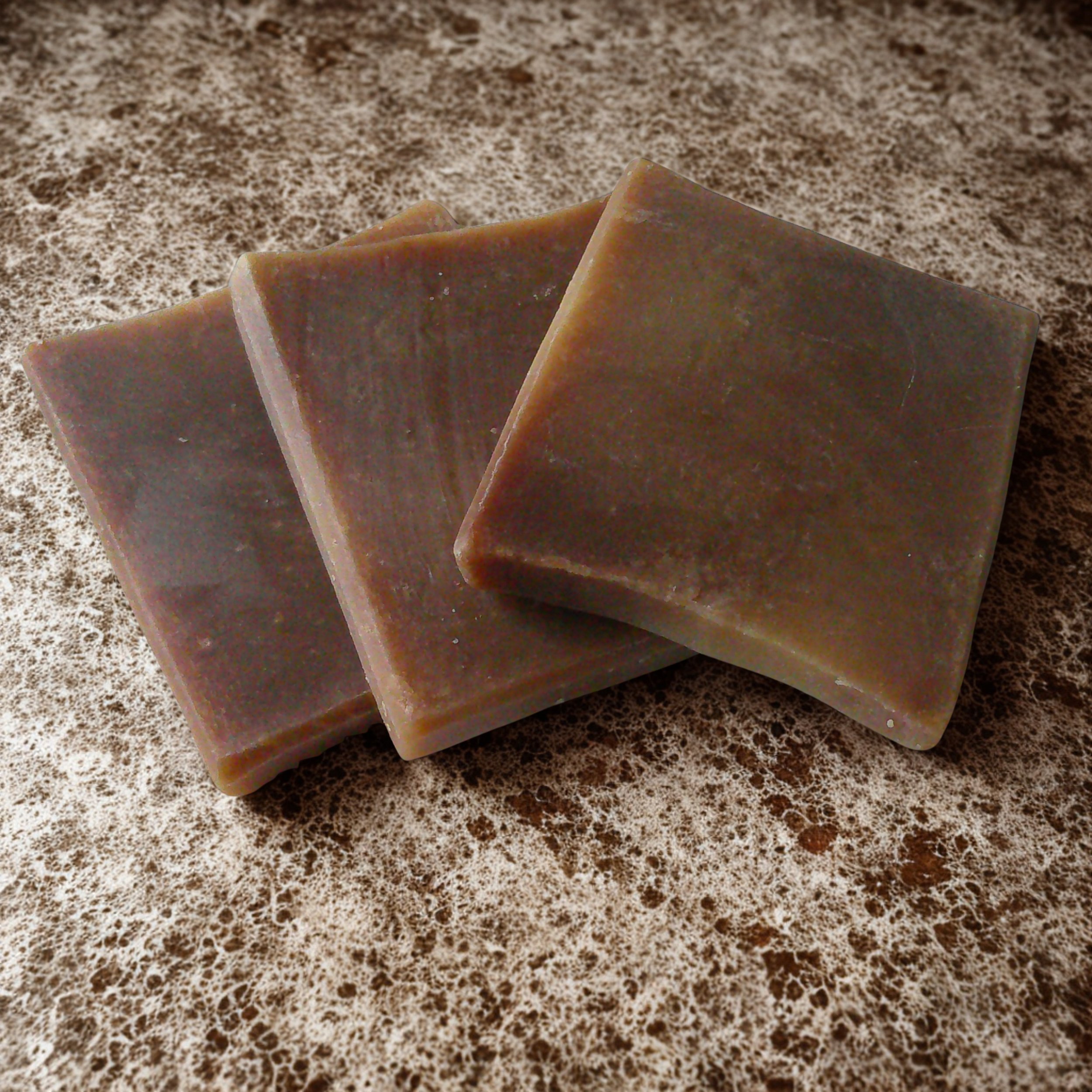 Three bars of brown soap on a speckled countertop.