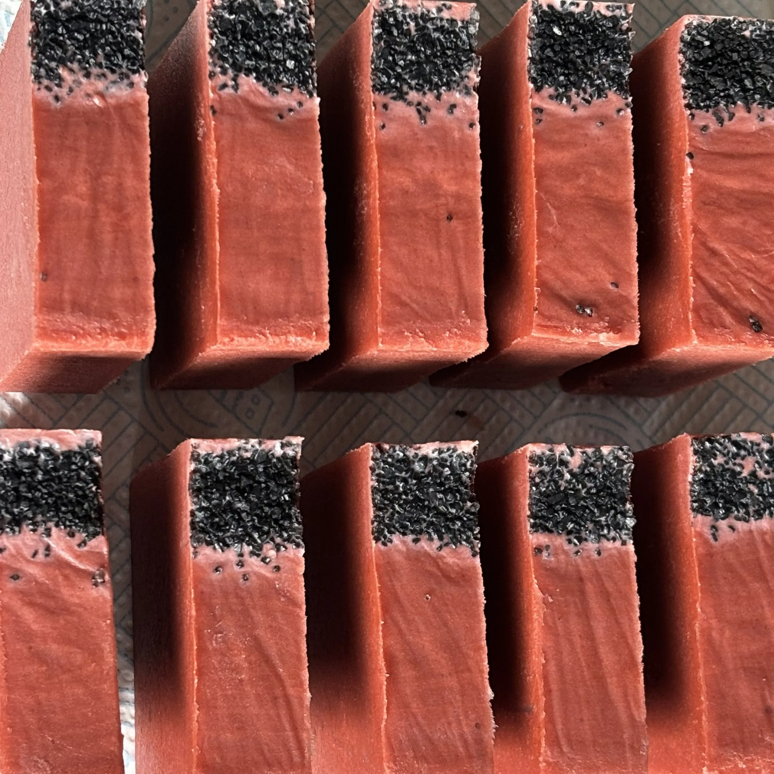 Close-up of strawberry bars topped with black sesame seeds, arranged in a row on a textured surface.