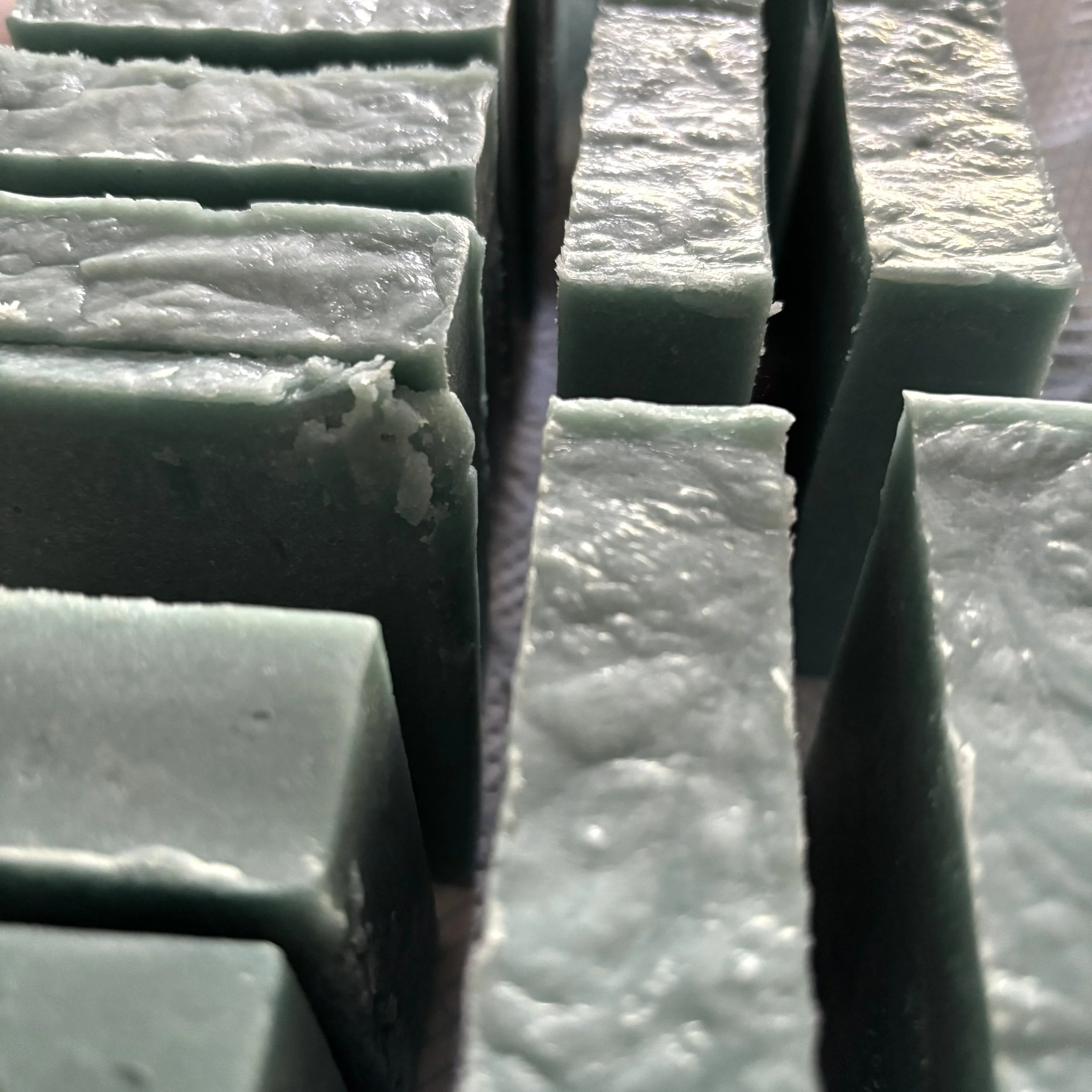 Close-up view of stacked rectangular blocks of soap with rough, textured surfaces, some with uneven edges, and a black object in the middle.