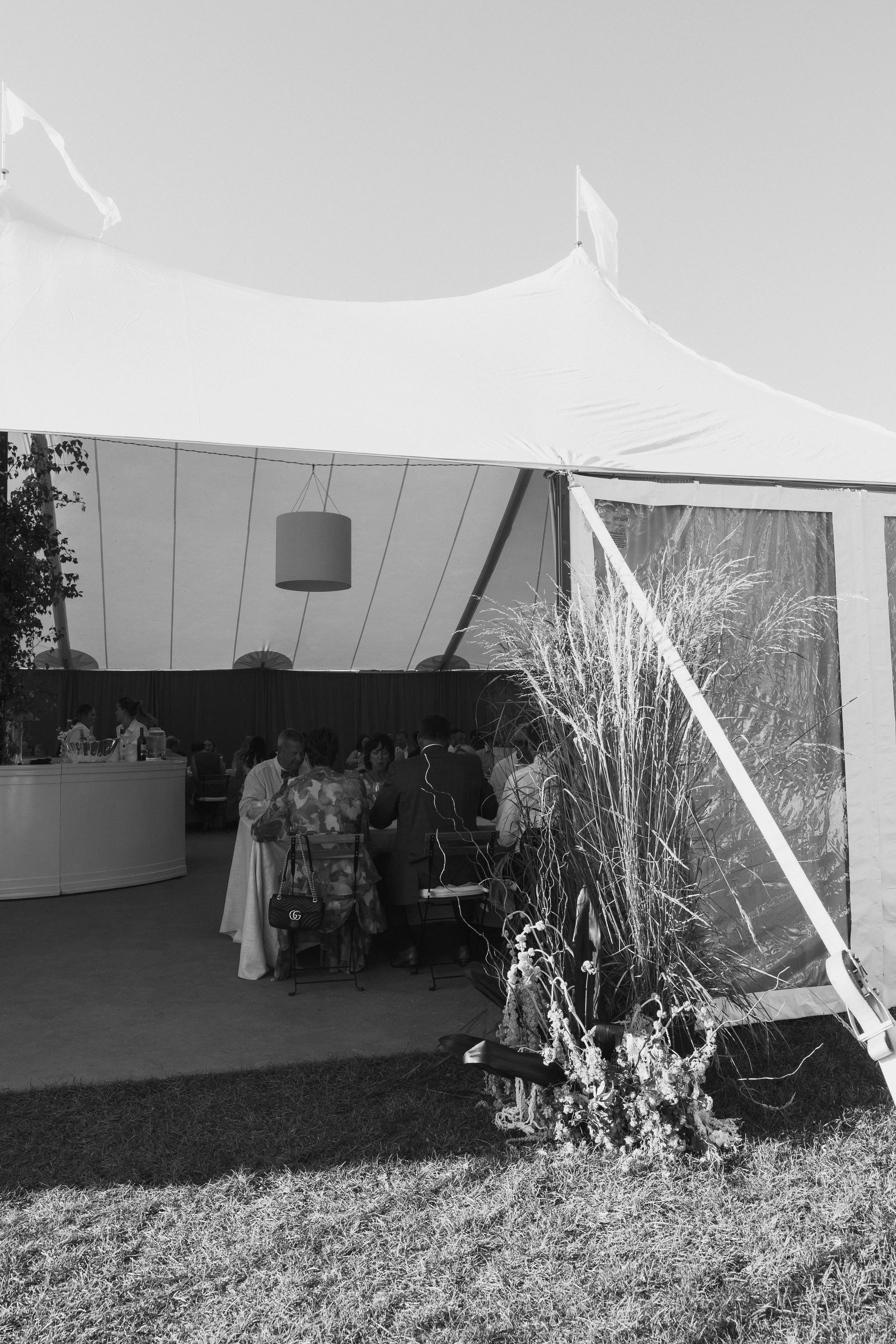 People sitting at a round table inside a large tent with floral decorations outside.
