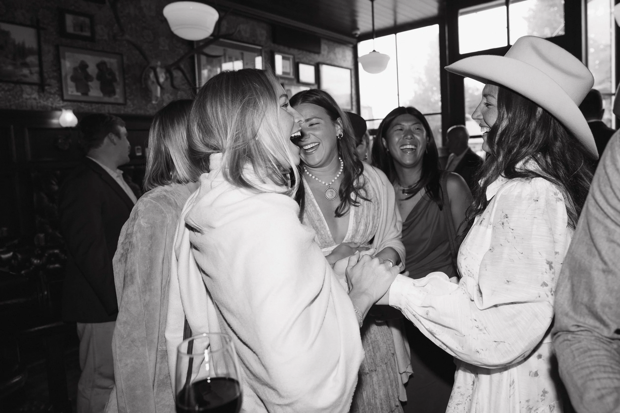A group of women laughing and holding hands at a celebration in a restaurant or bar.