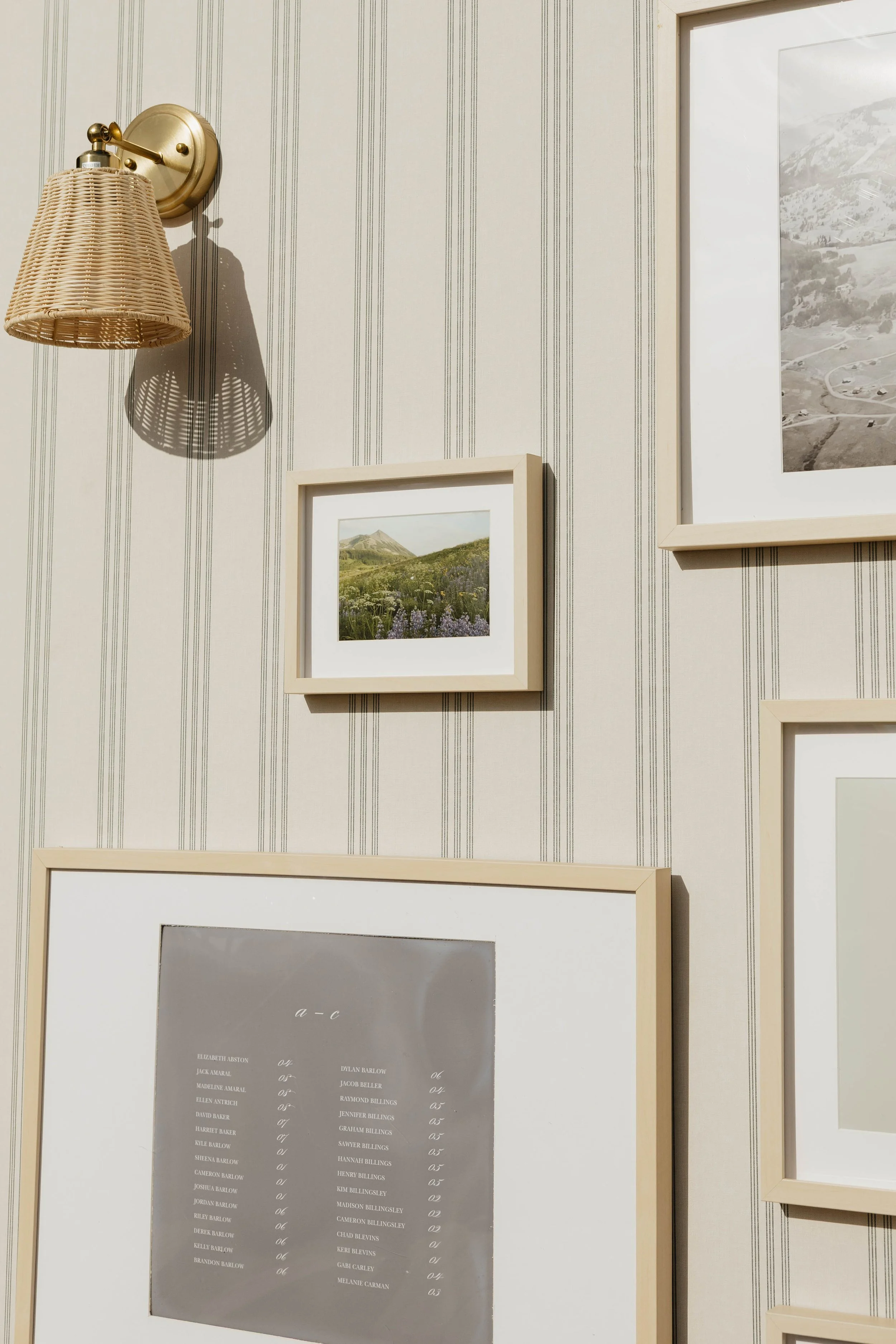 Interior wall with striped wallpaper, hanging picture frames, and a wall-mounted woven lampshade casting a shadow.