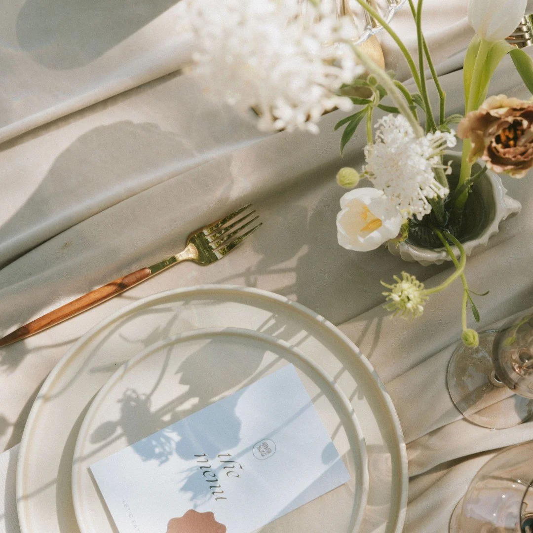 Table setting with a white plate, a gold fork with a marble handle, a floral arrangement in a white vase, and a card reading 'thank you 2023' on a cream-colored tablecloth.