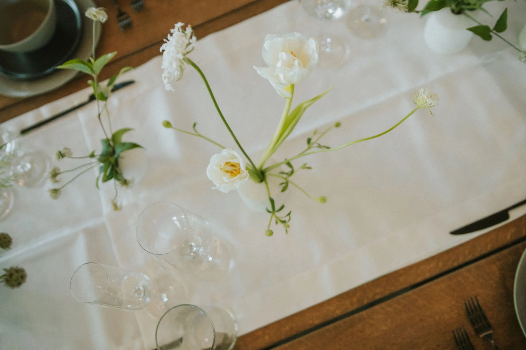 A white flower centerpiece with green leaves on a table with water glasses and silverware.