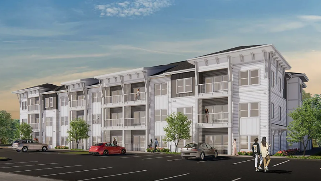 A modern multi-story apartment complex with balconies, has a parking lot in front with several cars, and a few people walking or sitting outside, trees and bushes surrounding the building.