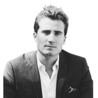 Black and white portrait of a man with dark, curly hair wearing a suit and open-collared shirt, looking serious at the camera.