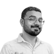 A man with glasses and a beard smiling, wearing a collared shirt, against a plain white background.
