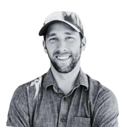 Black and white photo of a smiling man wearing a baseball cap and a button-up shirt.