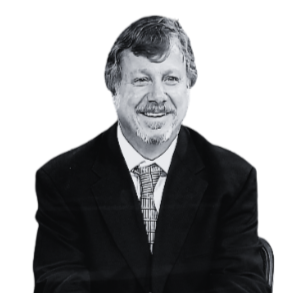 A black and white professional portrait of a smiling man with gray hair and a beard, wearing a dark suit and a tie.