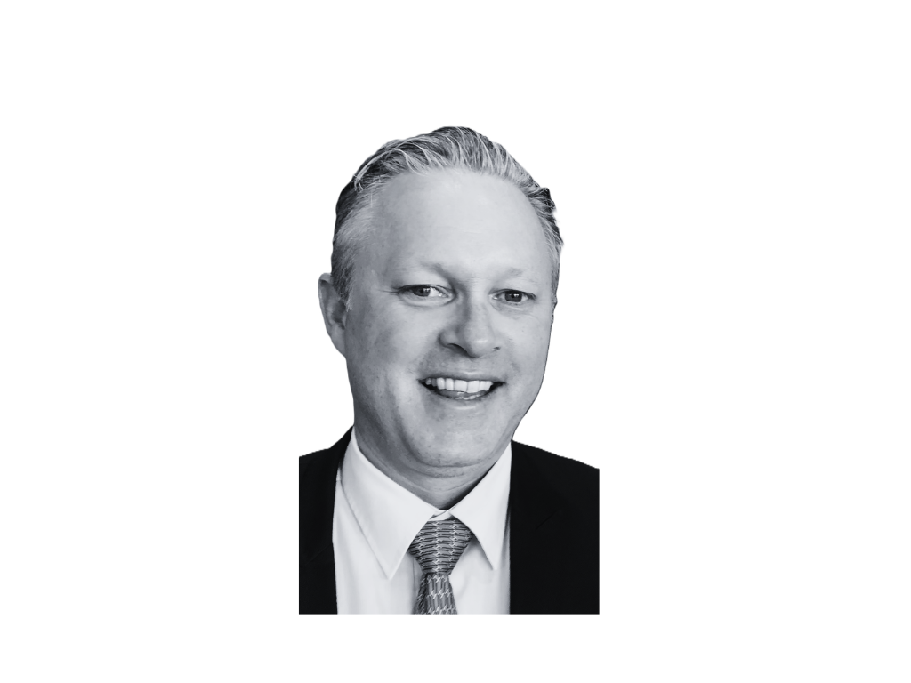 Black and white professional headshot of a smiling man with slicked-back hair, wearing a suit, shirt, and tie.