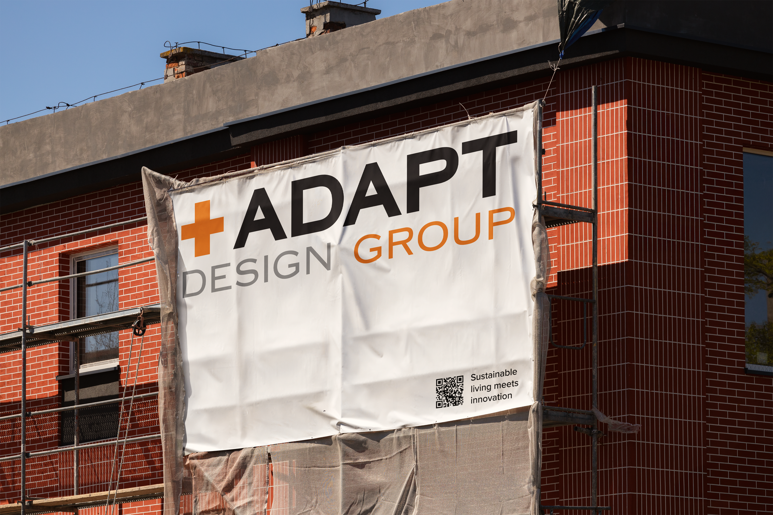 Construction site with a banner reading 'ADAPT DESIGN GROUP' on a brick building under construction.