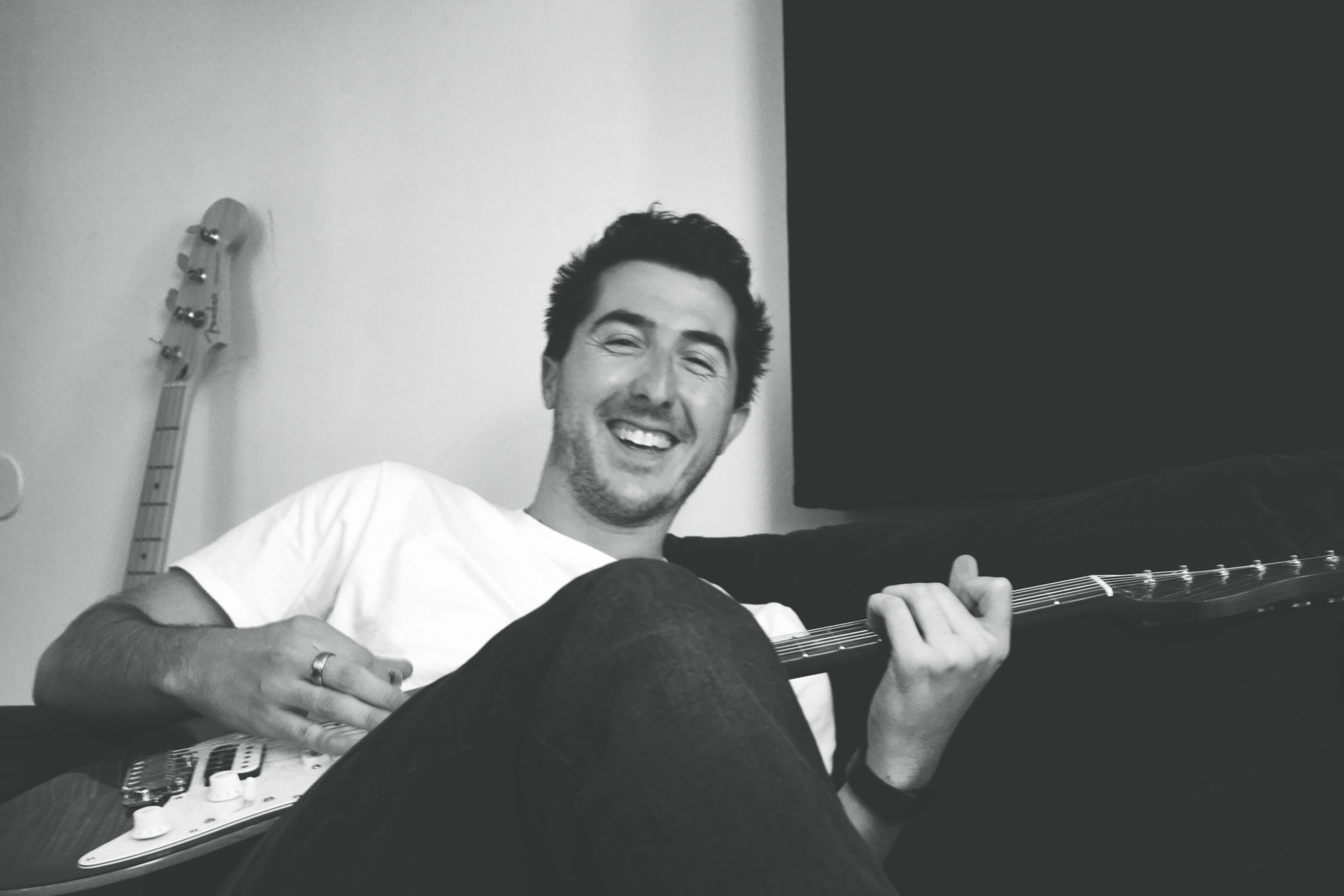 A man with dark, curly hair and a serious expression sitting in a room with a license plate on the wall and a black curtain behind him