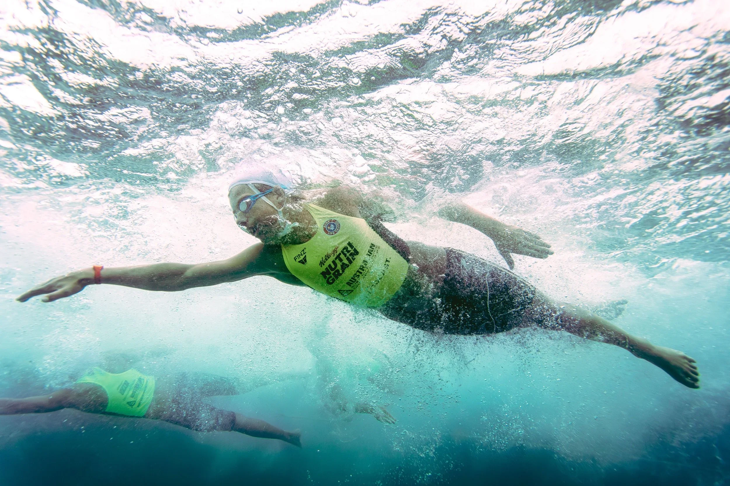A swimmer in a yellow wetsuit and goggles swimming underwater during a race.
