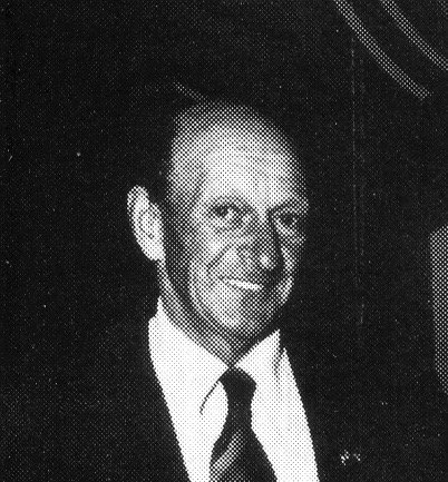 Black and white photo of a man in a suit and tie smiling.