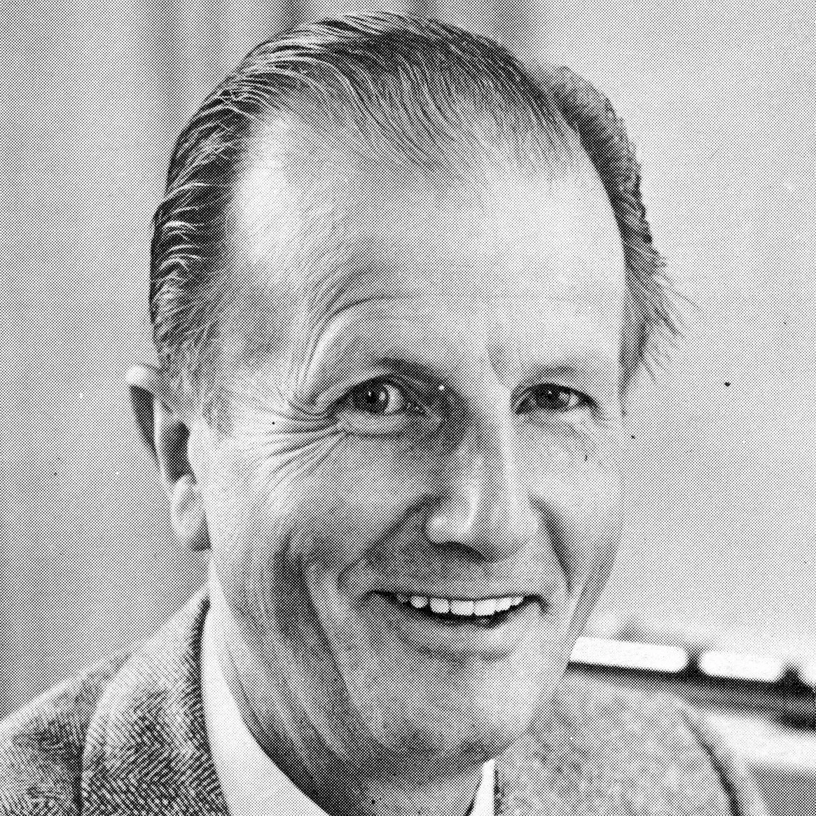 Black and white photograph of a smiling man with slicked-back hair, wearing a suit and tie.