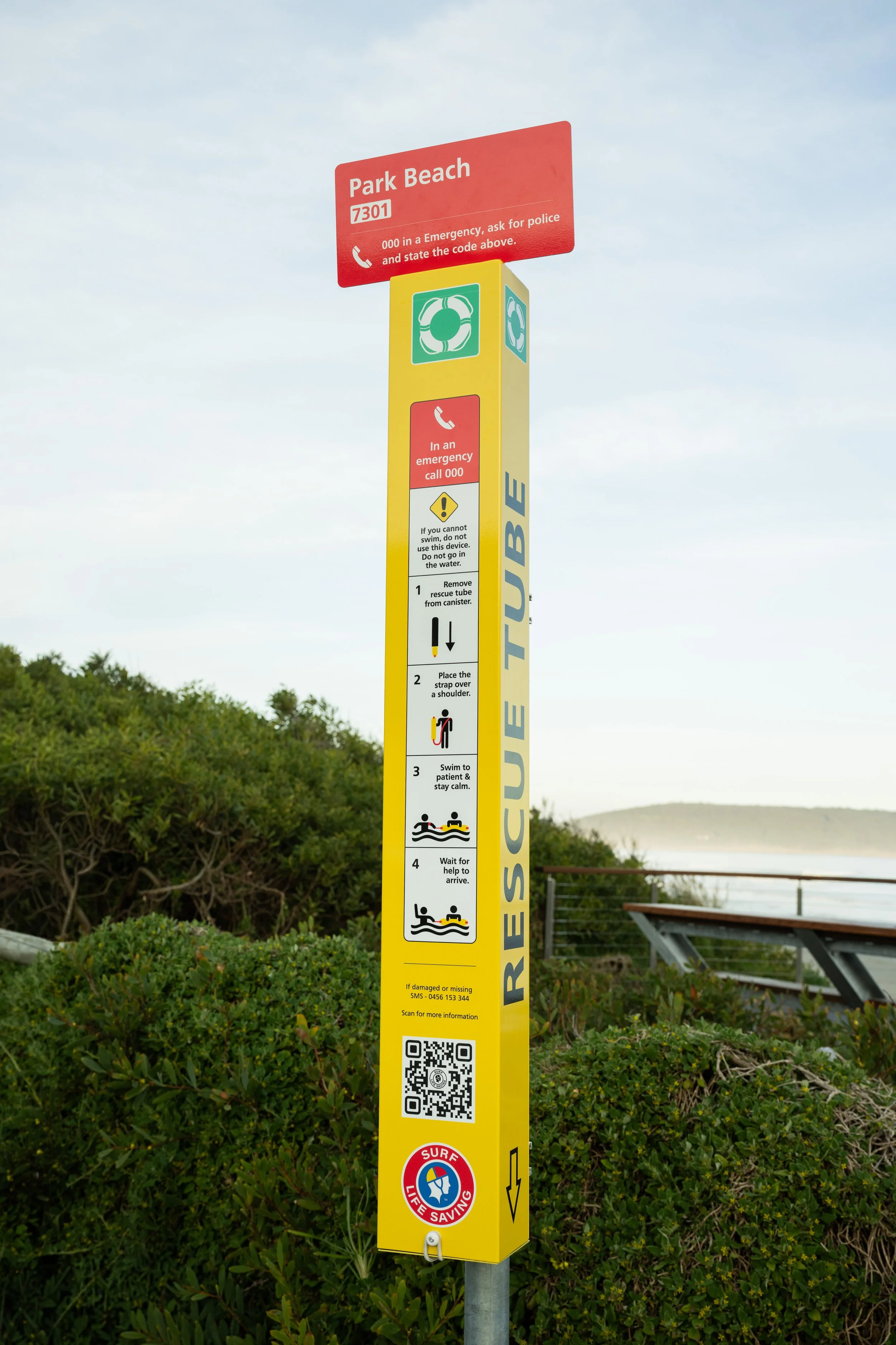 A yellow rescue tube station at a beach with step-by-step instructions for water rescue, including calling emergency services, removing the rescue tube from the canister, placing the strap over a shoulder, swimming to the patient and staying calm, and waiting for help.