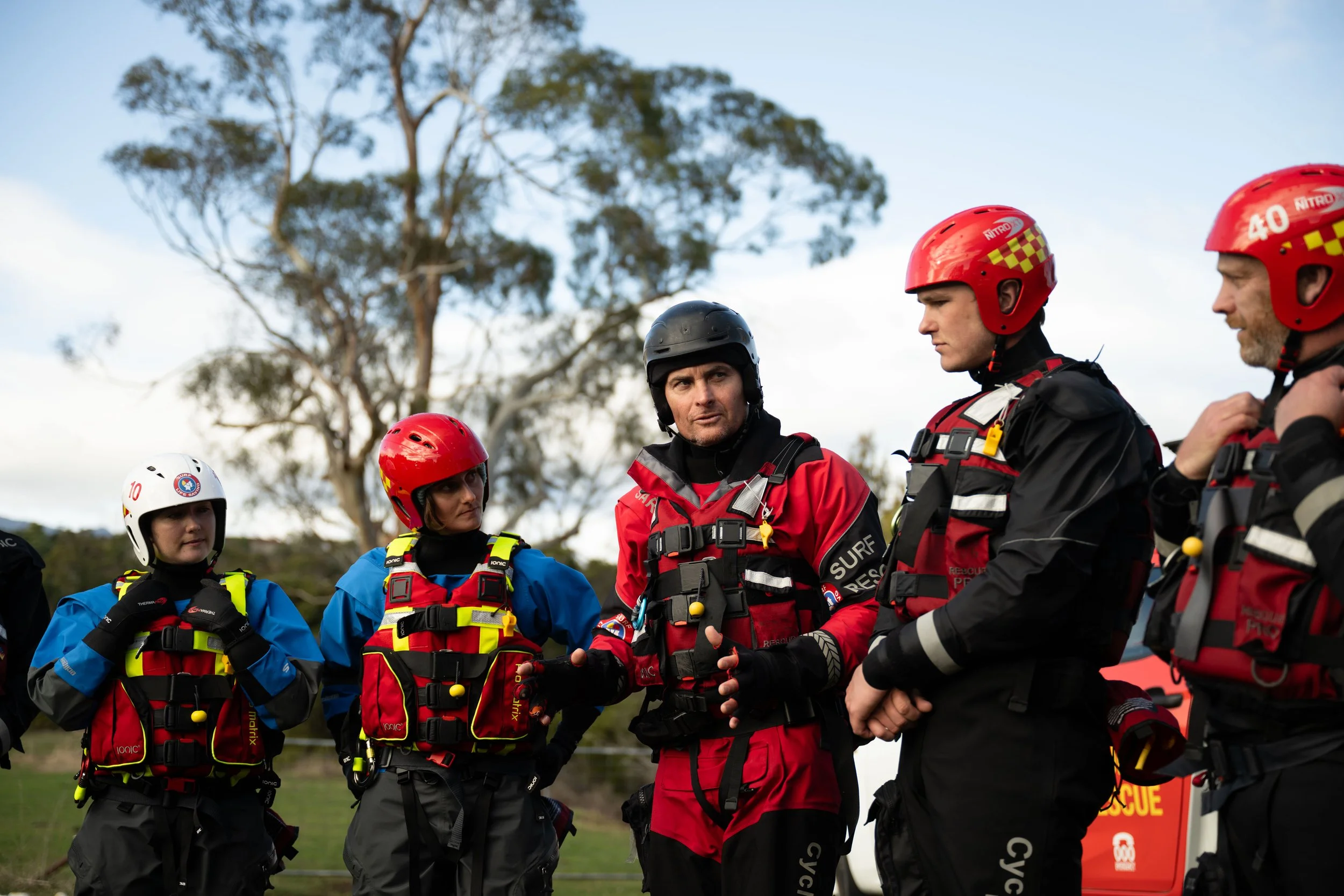 Group of rescue workers in uniform and helmets standing outdoors during daytime, engaged in a discussion.